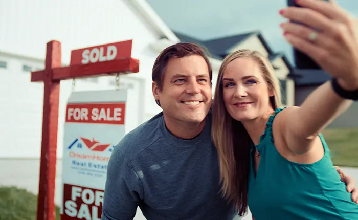 couple taking selfie in front of sold sign